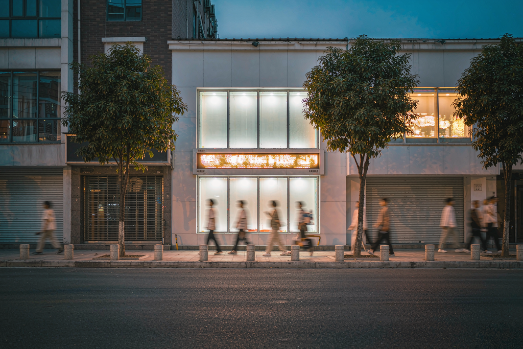 Row of storefronts at dusk with dot-matrix LED scrolling signs glowing in the shop windows