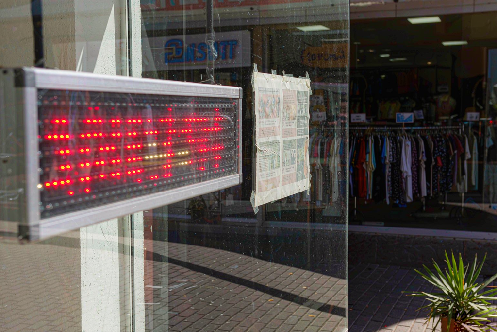 Bright red LED scrolling sign staying vivid in direct sunlight next to a faded printed paper poster