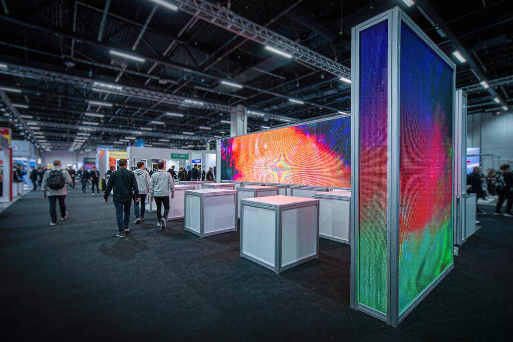 Trade show booth with a vertical column LED display and a wide flat video wall built from rental panels