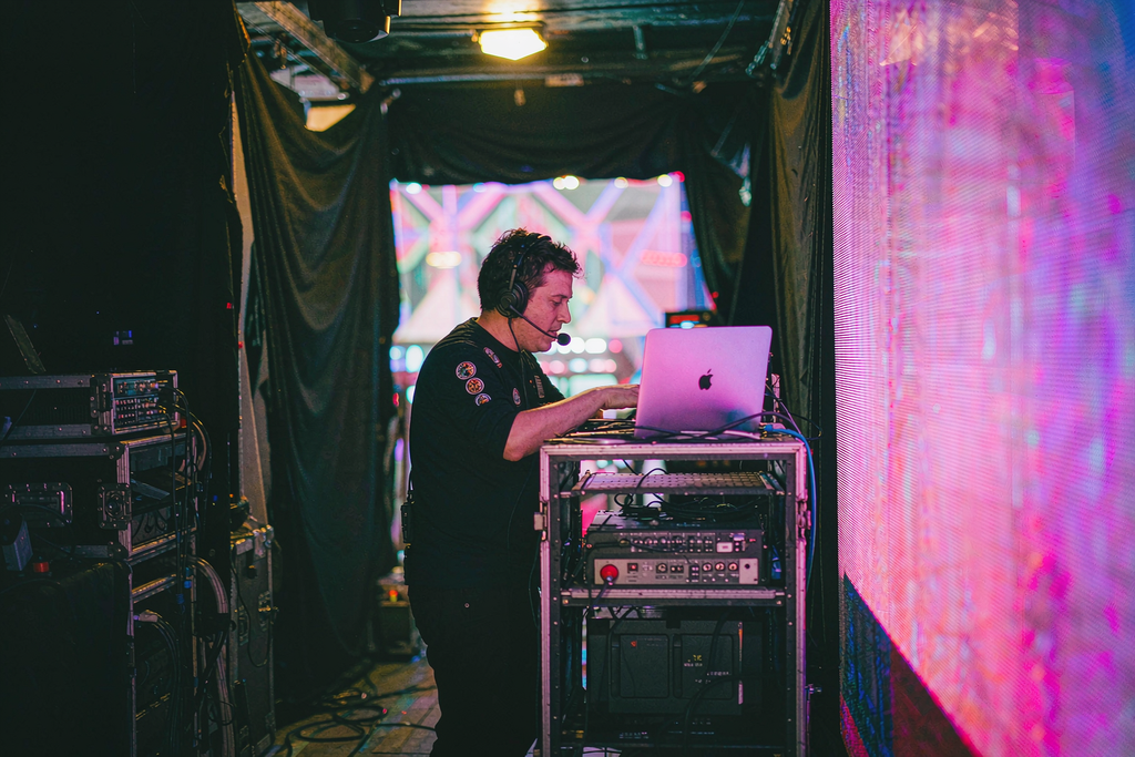 On-site AV technician with headset adjusting a video processor beside a glowing rental LED wall during a live event