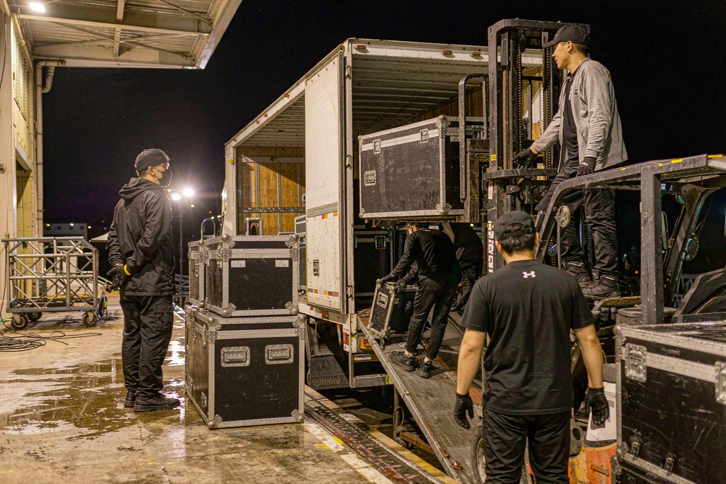 Crew loading flight cases with rental LED wall panels into a truck at a venue loading dock at night